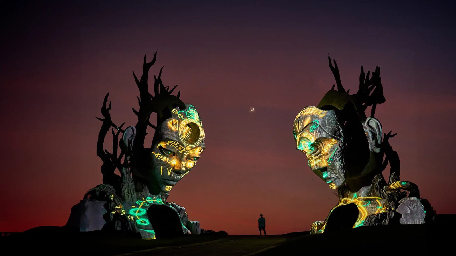 Two giant illuminated head sculptures facing each other at dusk at Nuanu Creative City